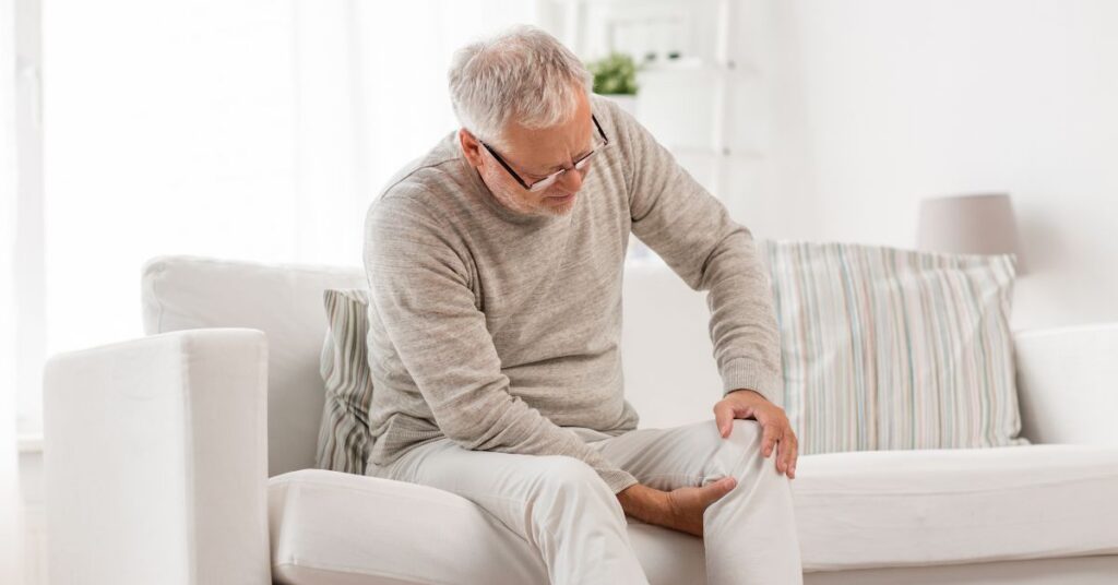man sitting on couch holding his knee